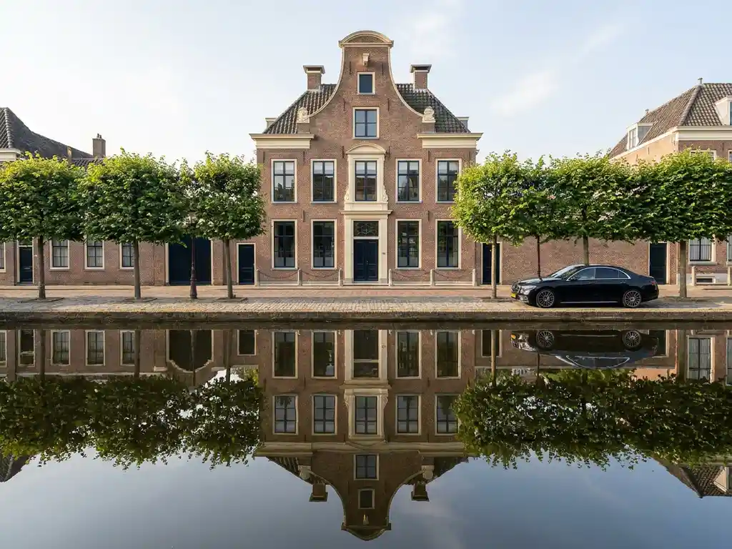 Elegant 17th-eeuws grachtenpand met trapgevel weerspiegeld in kalm kanaalwater, zwarte luxeauto geparkeerd langs geplaveide straat