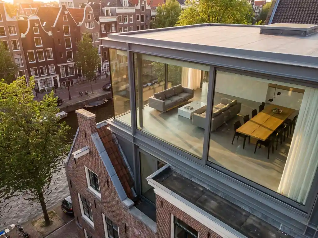 Glazen penthouse op Amsterdamse grachtenpand met minimalistisch interieur en uitzicht op historische gevelhuizen langs de gracht