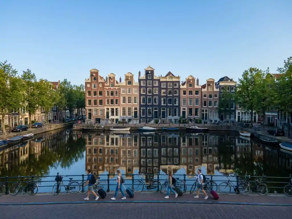 Amsterdamse grachtenpanden met trapgevels weerspiegeld in rustig water, jonge professionals wandelen langs geplaveide kade